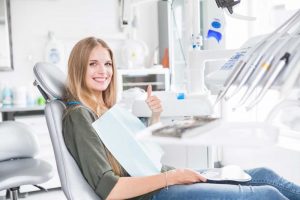 A woman sitting in a dentists chair giving a thumbs up.